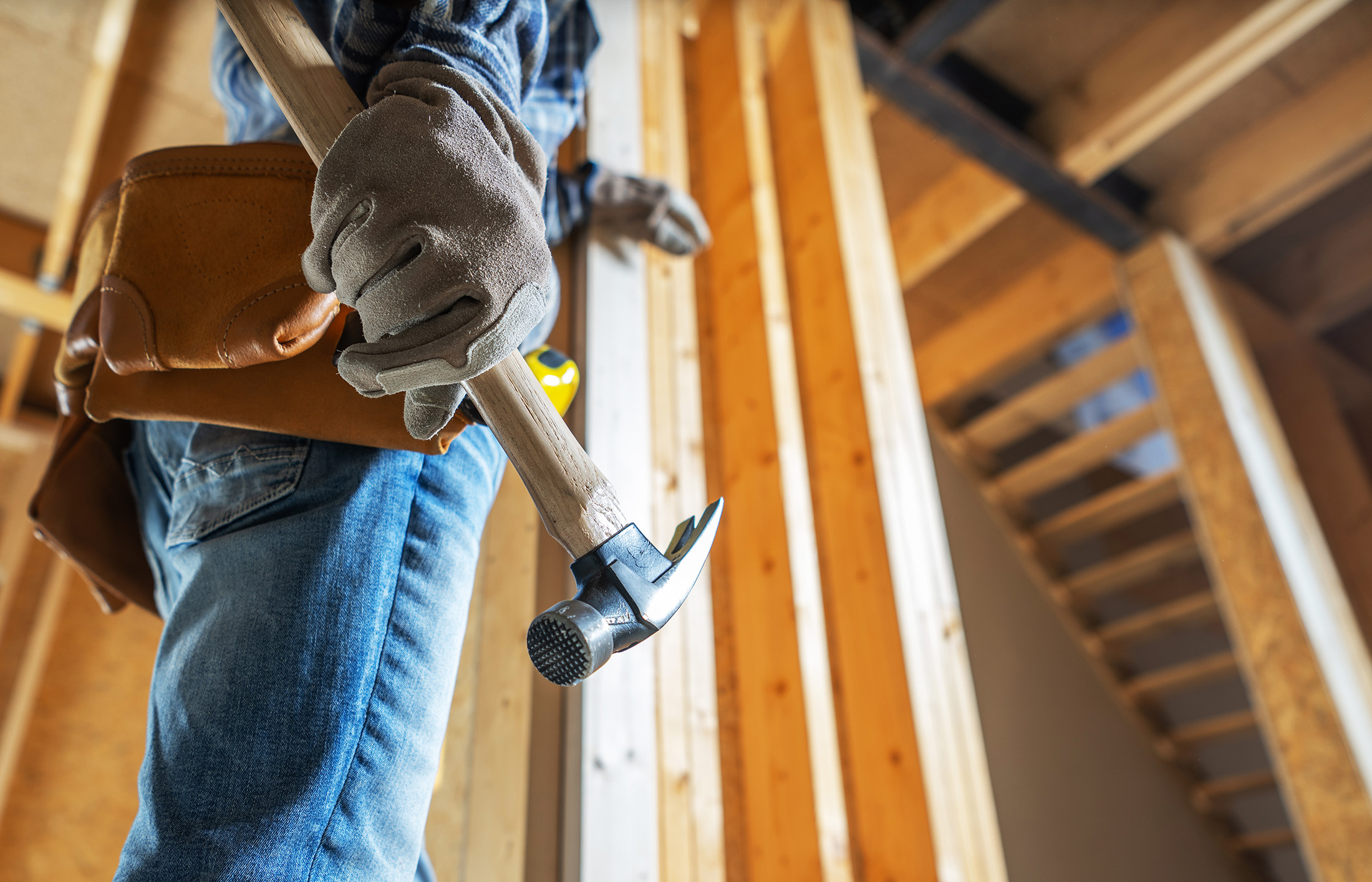 A construction worker grips a hammer and prepares to work on interior framing in a newly built home, showcasing the framing details and tools in use.